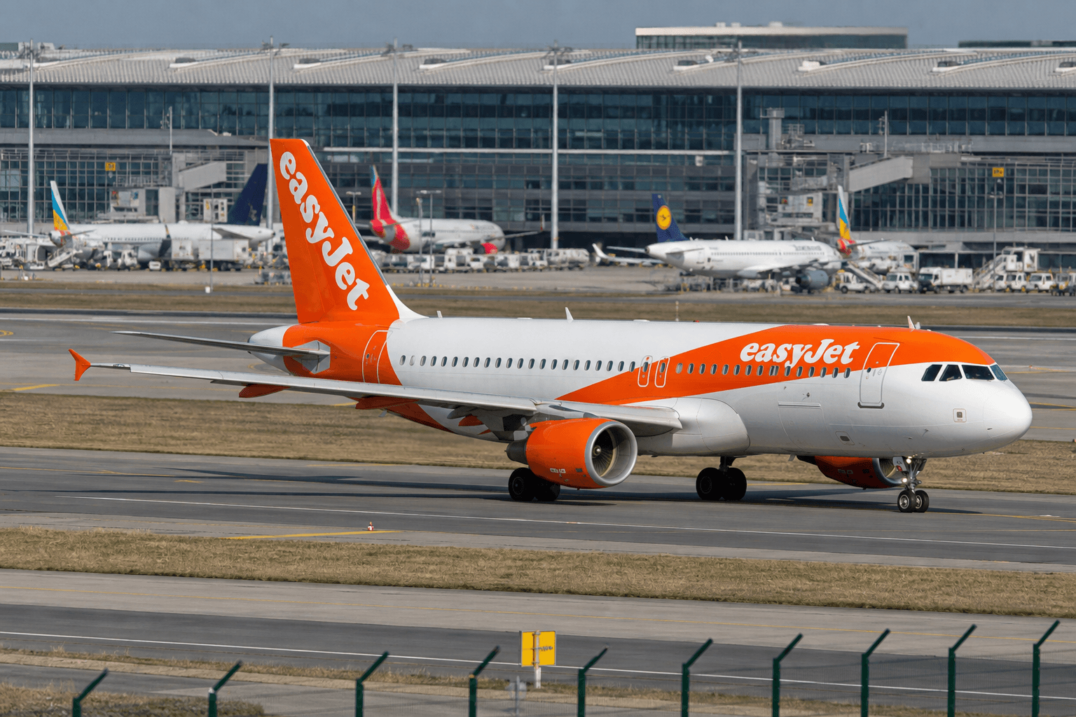 An EasyJet Airbus A320 taxiing on runway with terminal in background at daytime