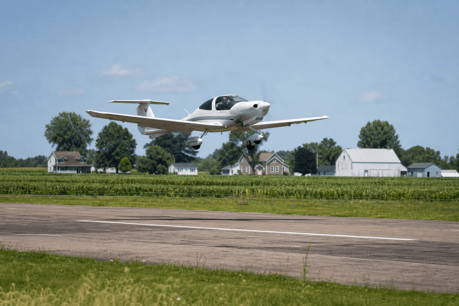 Small training aircraft operating from a rural airstrip surrounded by farmland and homes on a clear day