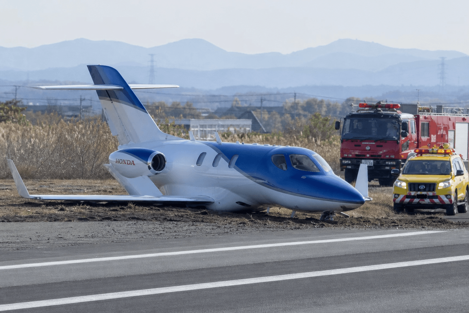 A HondaJet parked on a tarmac near a runway at a regional Japanese airport under overcast skies