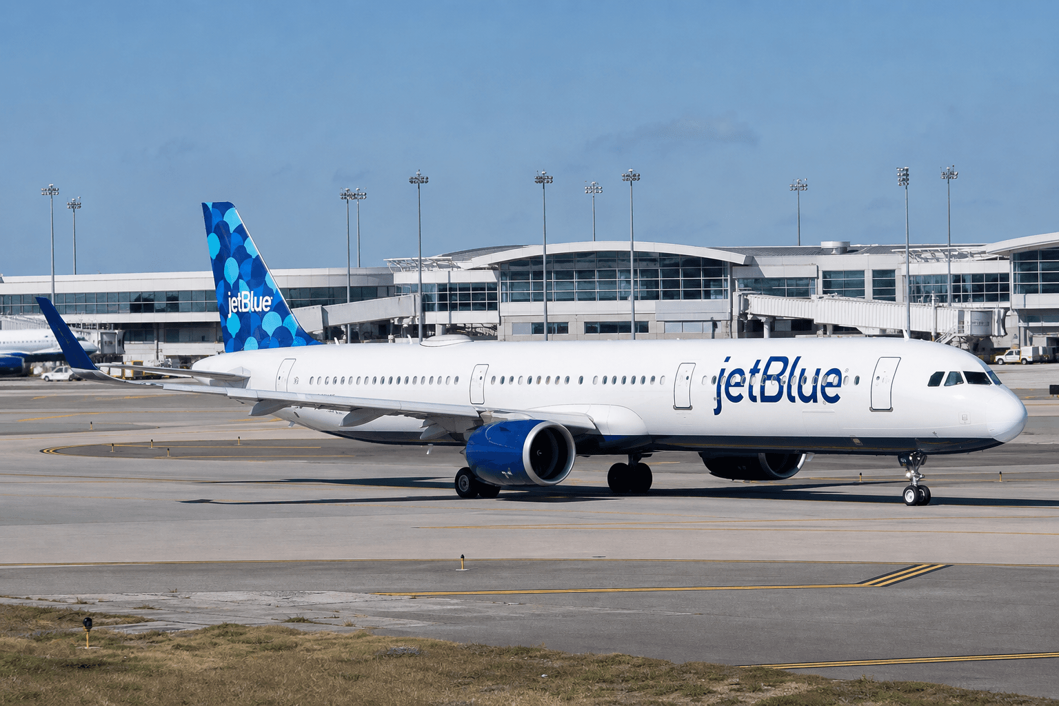 JetBlue aircraft taxiing under clear skies at a busy airport terminal