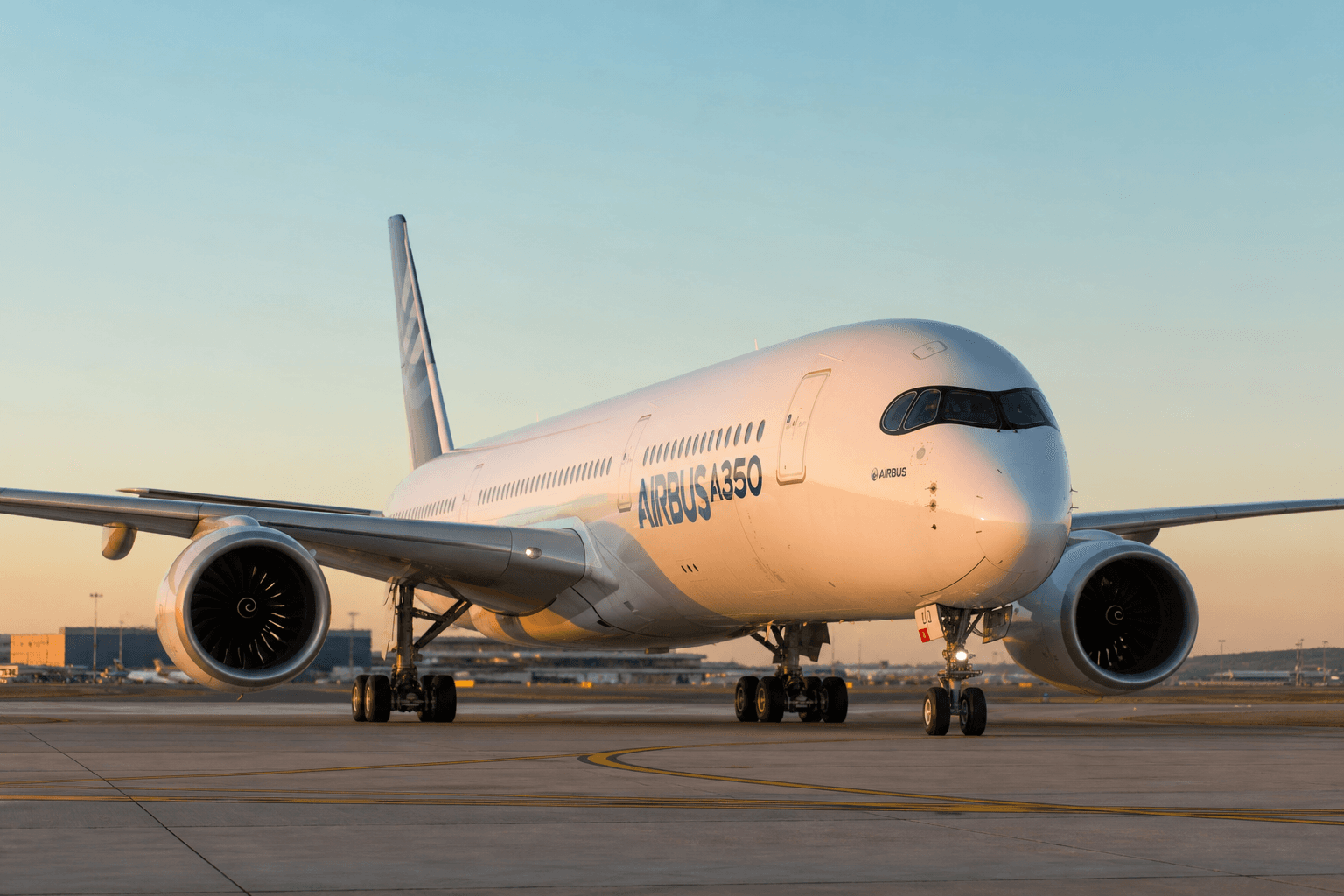 Airbus A350 widebody preparing for takeoff at sunset with hangars in background