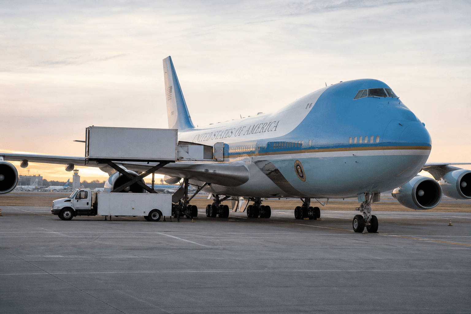 Boeing VC-25A Air Force One on tarmac with catering truck beside it at sunrise