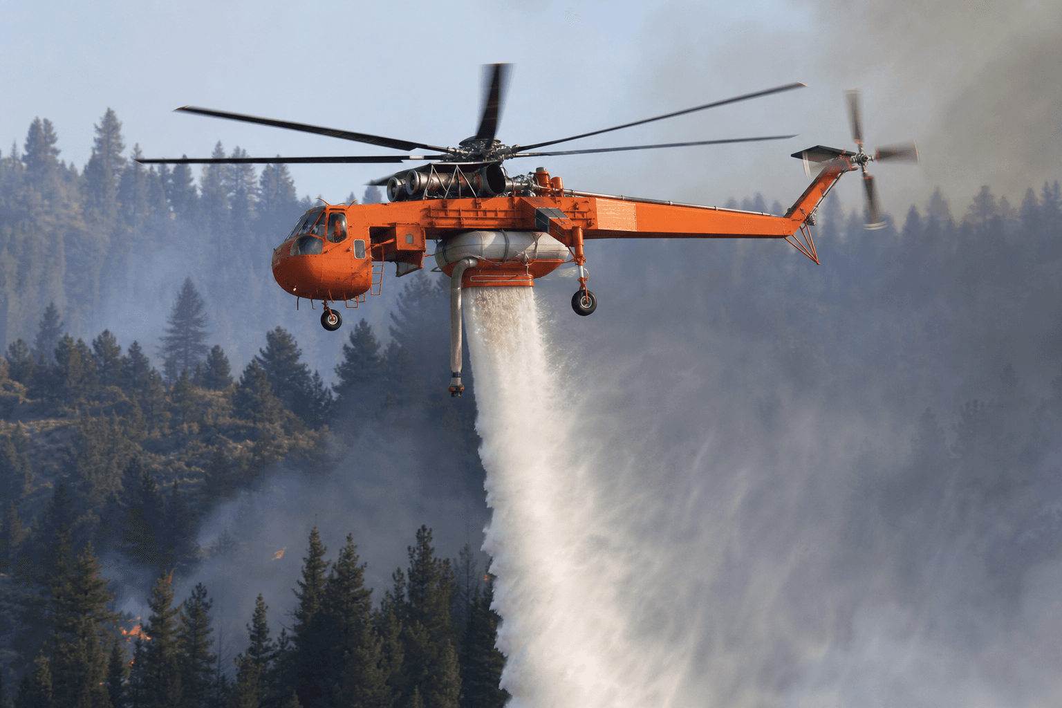 Sikorsky S-64 Skycrane hovering over forested terrain during firefighting operations in daylight