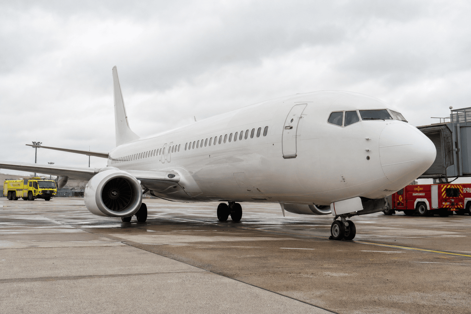 Boeing 737-800 on airport tarmac with emergency responders nearby under overcast sky