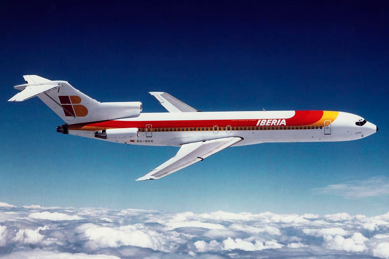 A Boeing 727 in flight over a busy US airport during daytime with clear weather.