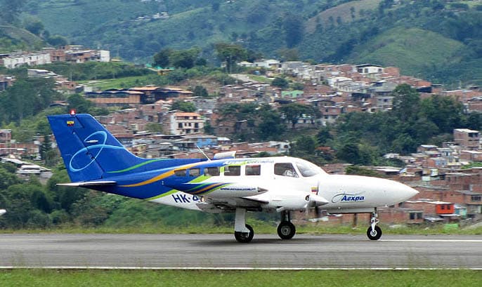 A Cessna 402 twin-engine aircraft taxiing at a tropical island airport with lush greenery
