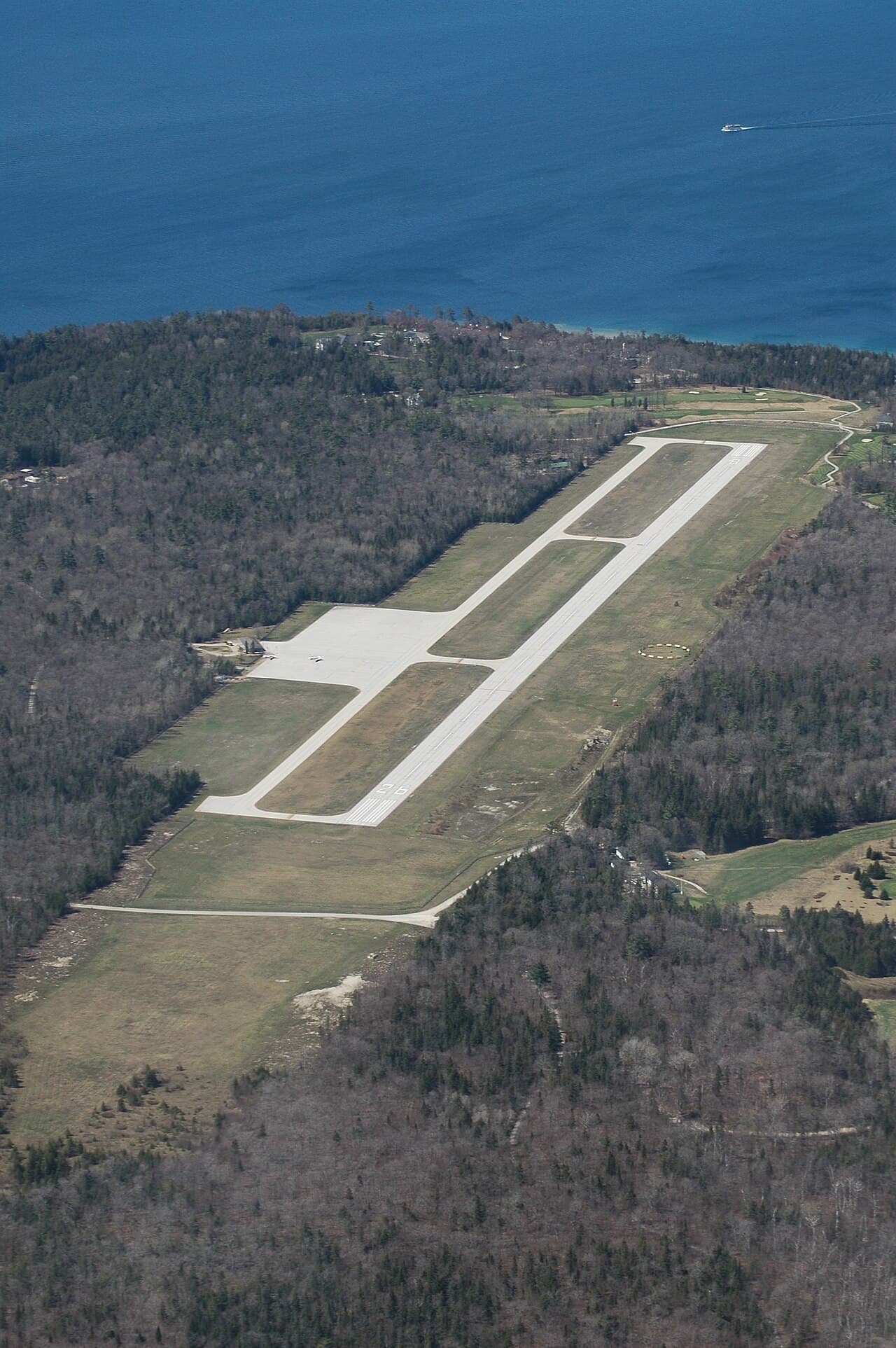 A small general aviation plane landing at a short runway overlooking water and forested terrain at Mackinac Island