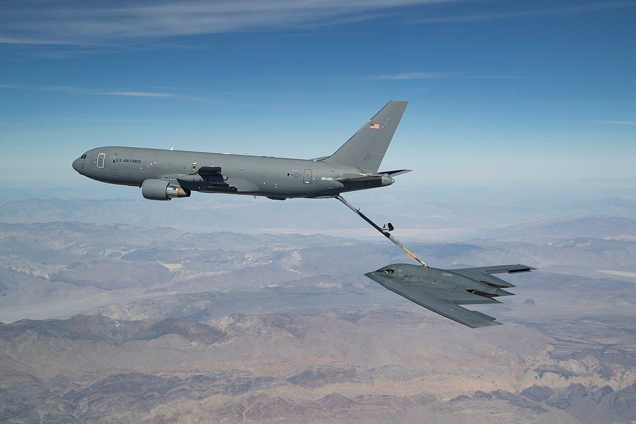 A Boeing KC-46 Pegasus tanker in flight with refueling boom extended against a clear sky