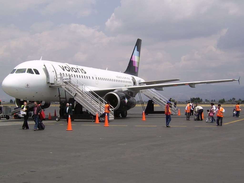 Commercial aircraft lined up at airport gates with terminal buildings in background during daytime