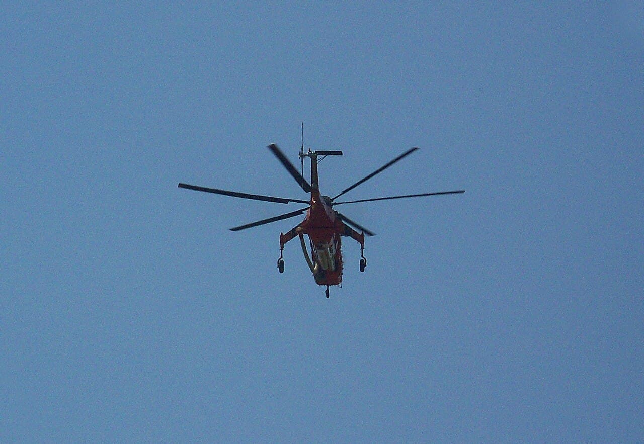 Sikorsky S-64 Skycrane hovering over forested terrain during firefighting operations in daylight